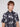 A young man with light brown hair models the Projek Raw BENJAMIN-BLACK shirt, featuring a navy palm tree print and wrinkle-resistant, 4-way stretch fabric. He stands against a plain light background, looking slightly to the side.
