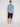 A man stands against a plain background wearing the Projek Raw BENJAMIN-BLUE 4-way stretch palm tree print shirt, paired with dark navy shorts and white sneakers. His left hand in his pocket highlights effortless comfort and style.