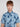 A young man with light brown hair models the BENJAMIN-BLUE short-sleeved palm tree print shirt by Projek Raw, made with 4-way stretch fabric, against a plain light background.