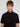 A young man with light brown hair and blue eyes wears the Projek Raw ALEXANDER-BLACK, a black wrinkle-resistant short-sleeve button-up shirt, standing against a plain light background and facing the camera with a neutral expression.