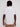 A person with short dreadlocks, wearing the ALEXANDER-WHITE shirt by Projek Raw and tan pants, stands with their back to the camera against a plain white background.