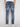 A person is shown from the back wearing Projek Raws GABRIEL-DISTRESSED INDIGO jeans and white shoes, standing against a plain light background.
