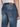 A person in Projek Raw GABRIEL-DISTRESSED INDIGO jeans and a white shirt, shown waist down from behind. The jeans feature two back pockets, a brown leather waistband patch, and the signature Baru fit.