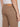 Close-up of a person wearing Projek Raw HUGO-DARK BEIGE colored denim jeans with back pockets and a tan leather waistband patch, paired with a white shirt. Their right arm is relaxed by their side.