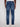 A person wearing Projek Raws NOLAN-INDIGO BLAST athletic fit jeans in indigo wash and white sneakers is shown from the back. The stretch-blend denim features two back pockets with stitching detail, set against a plain light background.