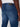 A person wearing Projek Raws NOLAN-INDIGO BLAST athletic fit jeans and a white shirt, shown from the back waist down. The jeans have two back pockets with visible stitching and a black leather patch on the waistband.