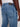 A close-up of a person wearing Projek Raw WYATT-INDIGO WASH jeans and a white shirt, highlighting the back pocket details and dark leather waistband patch. The brand’s signature style is visible, with the persons right arm at their side.