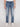 A person stands facing forward against a plain light background, wearing a white t-shirt, Projek Raw’s XANDER-DISTRESSED INDIGO jeans, and white sneakers.