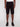 A person models the Projek Raw NATHANIAL-BLACK knee-length shorts, paired with a white shirt and black sneakers, standing against a plain light gray background. Only the lower half of the body is shown.