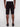 A person is seen from the back wearing Projek Raw NATHANIAL-BLACK knee-length shorts with rear pockets and a relaxed fit, paired with black shoes against a plain light background.