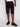 A person wearing Projek Raws PAULIN-BLACK knee-length cargo shorts with pockets and zippers, a white shirt, and black sneakers stands against a plain light background.