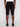 A person models Projek Raws PAULIN-BLACK cargo shorts, featuring side pockets and a just-below-the-knee fit, paired with black shoes and standing against a plain, light background.
