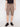 A person wears Projek Raw’s PAULIN-CASHEW taupe cargo shorts with a drawstring waist and side pockets, paired with a black t-shirt and black sneakers, standing against a plain light background.