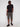 A man stands against a plain white background wearing Projek Raw DESMOND-OLIVE cargo shorts, paired with a black t-shirt and sneakers, one hand in his pocket and a relaxed expression.