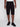 A person wearing Projek Raw JACOBI-BLACK cargo shorts with side pockets, a black belt, white t-shirt, and black sneakers stands against a plain light background. Image is cropped from shoulders to feet.