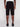A person is facing away from the camera, wearing Projek Raw JACOBI-BLACK cargo shorts with multiple pockets and button details, paired with a white shirt and black shoes. The background is plain and light-colored.