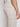 A person wearing Projek Raws DARIAN-NATURAL light beige pants with a side cargo pocket, viewed from the back and side, paired with a white shirt. The pants feature a linen-like fabric for a comfortable and stylish look.