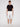 A person stands against a plain background wearing the DARIAN-WHITE shorts by Projek Raw, paired with a black t-shirt and white sneakers, looking straight at the camera with a neutral expression.