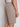A person wearing Projek Raw SYLVAIN-TABAC light brown textured shorts with a buttoned back pocket and a white shirt is shown from the waist down, facing away with their right hand by their side.