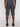 A person faces away from the camera, wearing Projek Raw REMINGTON-CHARCOAL knee-length shorts and black shoes, set against a plain light background.
