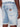 Someone stands with their hand by their side, wearing Projek Raw’s JOVIAN-BLEACH light blue denim shorts featuring rolled cuffs, visible back pockets, and a small brown leather patch on one pocket.