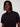A person with medium-length dreadlocks wears the ANDRÉ-BLACK short-sleeve button-up shirt by Projek Raw, standing against a plain light background and looking directly at the camera with a neutral expression.