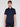 A person with short light brown hair wears the Projek Raw ANDRÉ-NAVY short-sleeve button-up shirt and dark pants, standing against a plain light gray background, facing forward with a neutral expression.