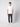 A young man with curly hair stands facing forward against a plain light background, wearing a white short-sleeve t-shirt, white sneakers, and PROJEK RAW Men’s Stretch Bungee Cargo Jogger in dark gray.