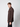 A young man with light brown hair models the PROJEK RAW Mens Long Sleeve Casual Dress Shirt in dark brown, paired with black pants and standing sideways against a plain light background, looking at the camera.