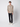 A young man with short curly hair and a neutral expression wears the PROJEK RAW Mens Long Sleeve Plaid Button-up Shirt in beige and brown, styled with black pants and white sneakers, standing against a plain light background.