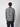 A man with curly brown hair stands with his back to the camera, wearing a PROJEK RAW Mens Long Sleeve Plaid Button-up Shirt in grey, white, and blue tones, plus dark cargo pants, against a plain light background.