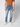 A person wears PROJEK RAW Mens 5-Pocket Straight Fit Jean in light blue, a brown short-sleeve shirt, and white sneakers, standing against a plain light gray background. The photo is cropped from the shoulders down.