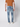 A man in a brown T-shirt and white sneakers stands facing away, displaying the back of the PROJEK RAW Mens 5-Pocket Straight Fit Jean against a plain light background.