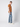 A man stands sideways in a brown T-shirt, PROJEK RAW Mens 5-Pocket Straight Fit Jean, and white sneakers against a plain light gray background.