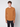 A young man with short curly hair wears the PROJEK RAW Mens Long Sleeve Crewneck T-shirt in brownish-orange, paired with dark jeans and standing against a plain light gray background—a true wardrobe essential.