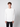 A young man with curly brown hair wears the PROJEK RAW Mens Long Sleeve Henley Top in white, paired with black pants, standing against a plain light gray background.
