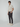 A young man stands against a plain background, wearing a short-sleeve beige button-up shirt, PROJEK RAW Mens Solid Bungee Cargo Pant with cargo pockets, and white sneakers. He gazes to the side with a neutral expression, exuding a casual streetwear vibe.