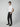 A young man stands sideways with one hand in his pocket, wearing a plain white tee and PROJEK RAW Mens Solid Bungee Relaxed Chino Pant, paired with black slip-on shoes against a light gray studio background.