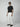 A man stands slightly turned against a light gray background, wearing PROJEK RAW Mens Solid Bungee Loose Chino Pant, a black t-shirt, black slip-on shoes, and sunglasses.