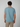 A man with short curly hair, seen from behind, wears a light blue PROJEK RAW Mens Short Sleeve Crew Neck T-shirt and beige pants—an effortlessly stylish addition to any casual wardrobe—set against a plain light gray background.