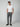 A man stands against a plain background wearing a white t-shirt, PROJEK RAW Mens Drawstring Bungee Plaid Chino Pant in gray, and black slip-on shoes, his hands in his pockets and looking relaxed.