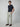 A man stands against a plain background, wearing a dark navy t-shirt, brown loafers, and PROJEK RAW Mens Textured Bungee Melange Chino Pant in light gray made from stretch fabric. His hands are in his pockets as he faces slightly to the side.