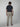 A man with brown hair, wearing a navy short-sleeve shirt, PROJEK RAW Mens Drawstring Linen Pant in light beige, and brown shoes stands facing away from the camera against a plain light gray background.