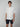 A young man models the PROJEK RAW Mens Short Sleeve Shirt with Floral Print—white, button-up, and paired with dark shorts—standing against a plain background with a neutral expression and relaxed posture.