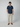 A man with short curly hair stands facing forward in a PROJEK RAW Mens Short Sleeve Textured 4-Way Stretch Shirt (dark blue), light beige pants, and brown boat shoes, posed against a plain light gray background.