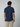 A man with short brown hair stands with his back to the camera, wearing a PROJEK RAW Mens Short Sleeve Textured 4-Way Stretch Shirt in dark blue and beige pants against a plain light gray background.
