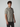 A young man with short curly hair wears the PROJEK RAW Mens Short Sleeve Textured 4-Way Stretch Shirt in light gray and dark pants, standing against a plain light background and looking slightly to the side.