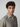 A young man with curly brown hair and light eyes, wearing a PROJEK RAW Mens Short Sleeve Textured 4-Way Stretch Shirt in beige with a subtle pattern, stands against a plain light background.