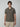 A young man with straight brown hair models the PROJEK RAW Mens Short Sleeve Textured 4-Way Stretch Stripe Shirt and beige pants, standing against a plain light gray background.