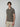 A young man with medium-length brown hair wears the PROJEK RAW Mens Short Sleeve Textured 4-Way Stretch Stripe Shirt in olive green, paired with light beige pants. He stands against a plain light gray background, gazing slightly to the side.